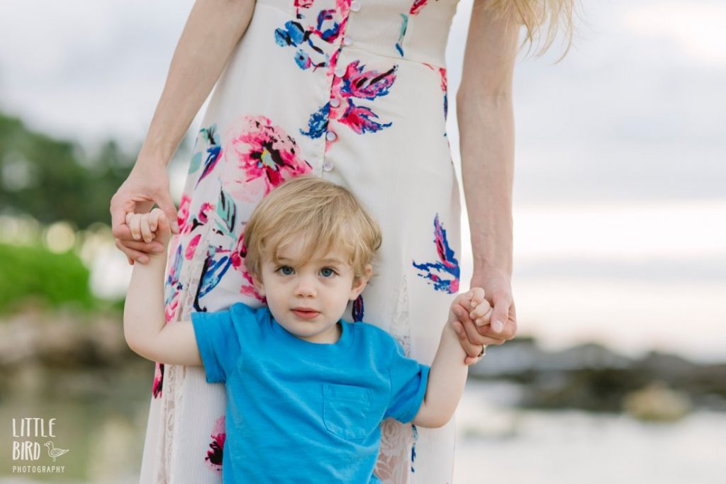 mom holding onto little boy's hands as they play in the water in hawaii