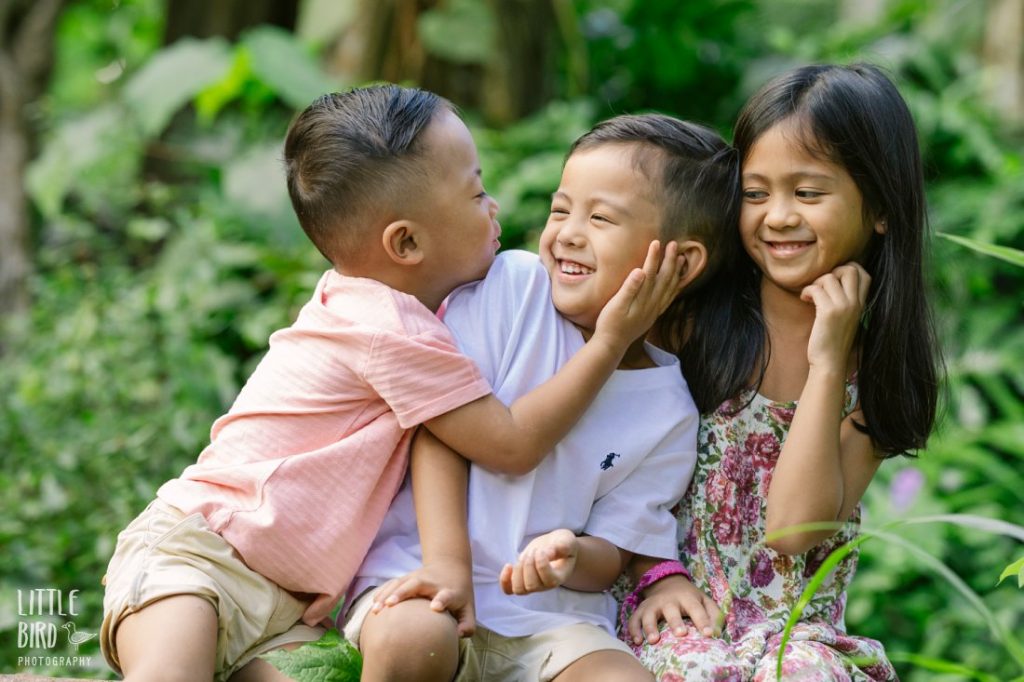siblings trying to share a kiss during a family photo shoot in hawaii